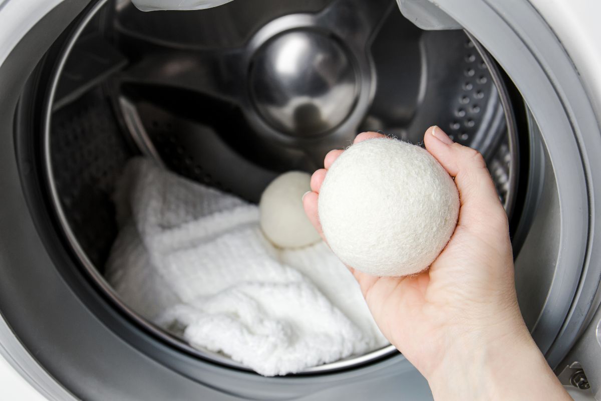 A bamboo pillow and several dryer balls are placed inside a dryer on a low heat setting.